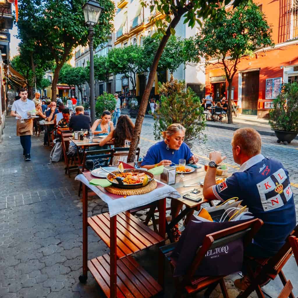 Toeristen zitten in een restaurant paelle te eten aan een terras in Sevilla